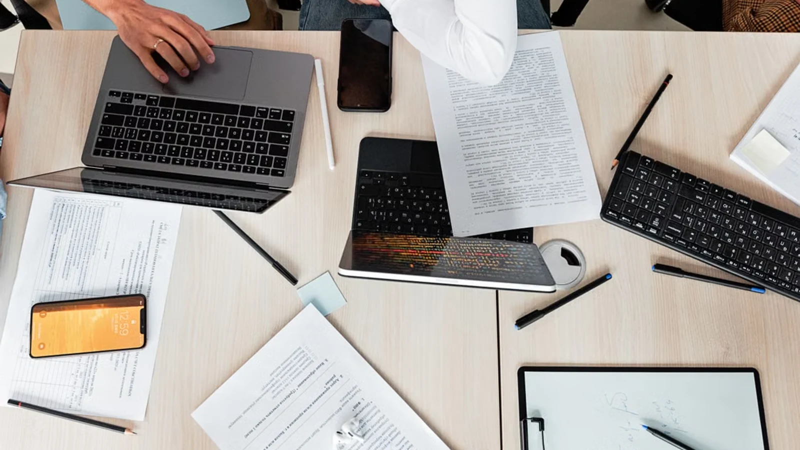 Overhead workspace with laptops, printed documents, phones, and writing tools